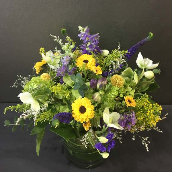 Low mixed arrangement of yellow and purple flowers in a round clear glass vase