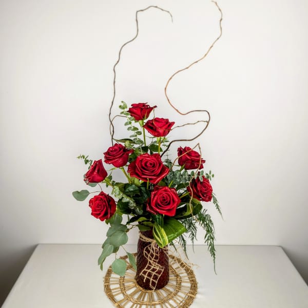 Red roses arranged in a tall vase with curly branches
