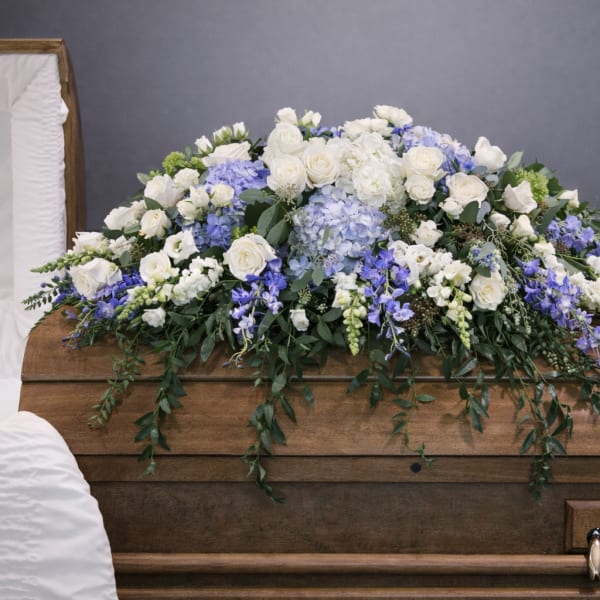 White and blue floral casket spray on a wooden casket