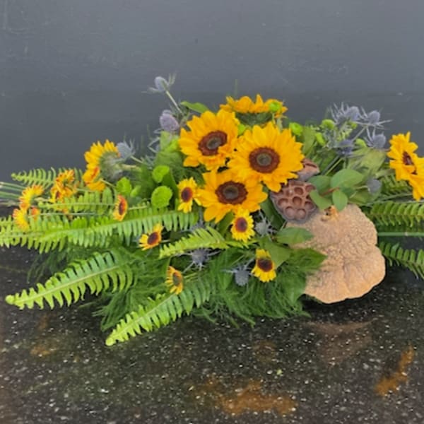 Sunflower arrangement with ferns and decorative pods on a low base
