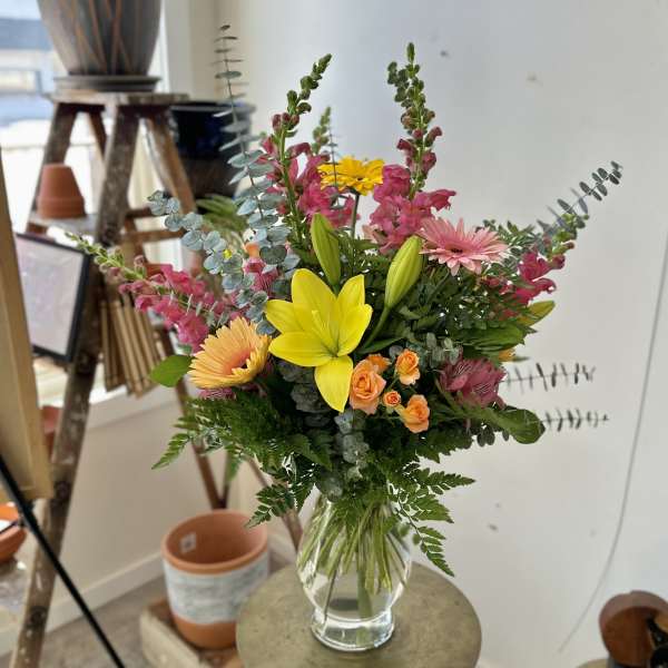 Mixed bouquet with yellow lilies, pink gerberas, and orange roses in a clear vase