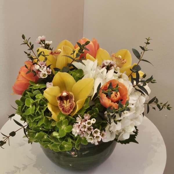 Mixed bouquet of yellow and orange flowers in a dark bowl vase