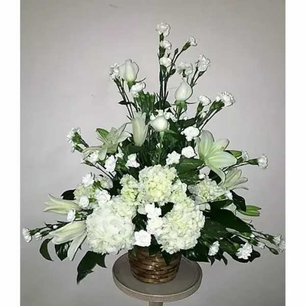 White floral arrangement in a woven basket with lilies and carnations