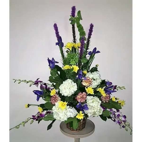 Tall mixed flower arrangement in a basket with purple, white, and yellow blooms