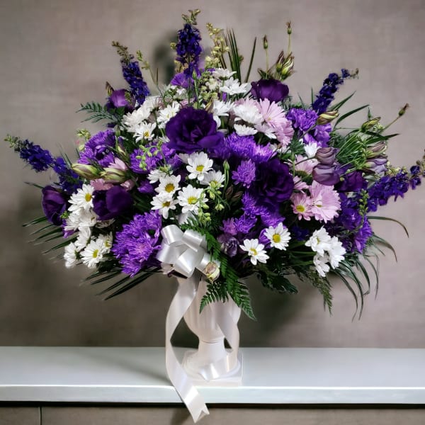 Purple and white mixed flower arrangement in a white vase with ribbon