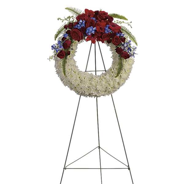 Circular funeral wreath of red and white flowers on a metal stand