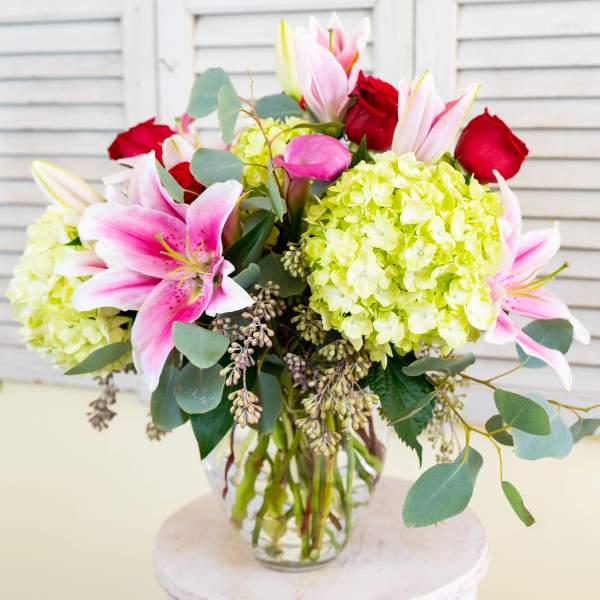 Bouquet of pink lilies, red roses, and green hydrangeas in a glass vase