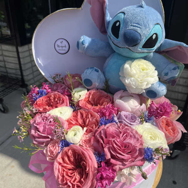 Heart-shaped box with a Stitch plush and pink and white flowers