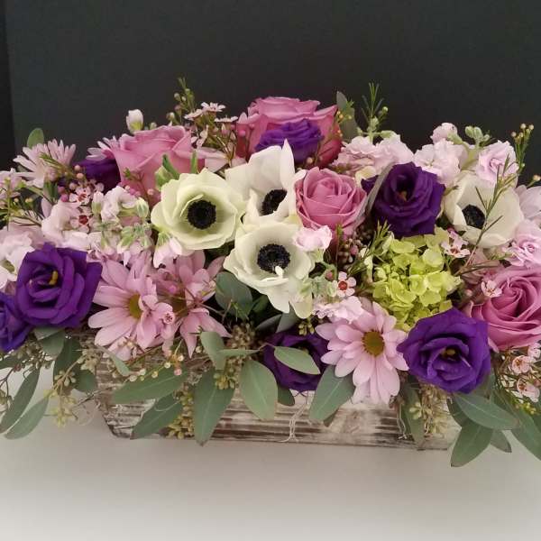 Mixed pink, purple, and white flowers in a low rectangular wooden container