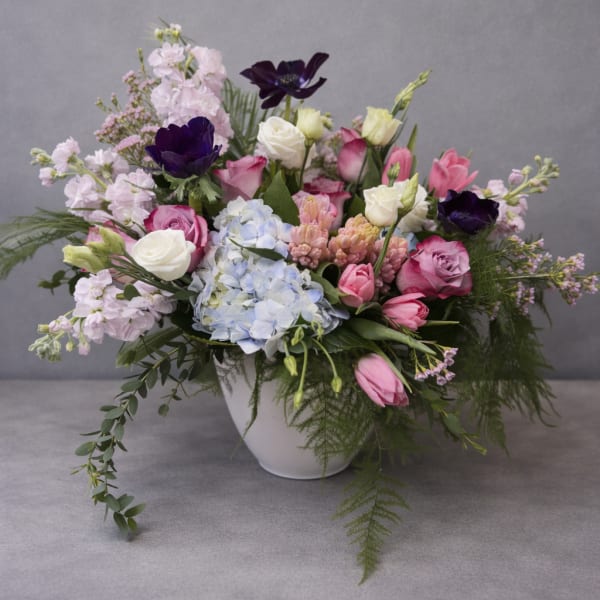 Mixed pink, white, and purple flowers arranged in a white bowl vase