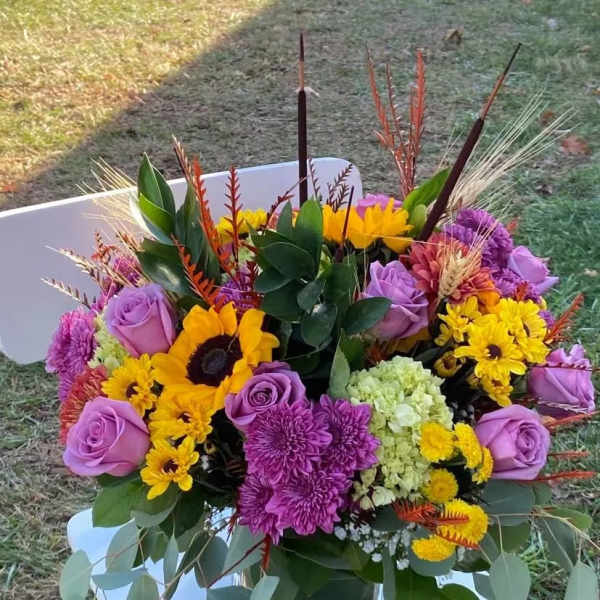 Colorful bouquet with purple roses, yellow sunflowers, and chrysanthemums in a glass vase