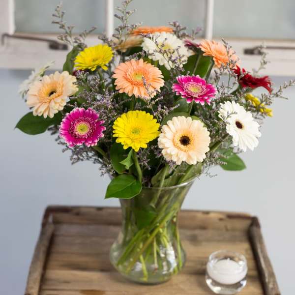 Mixed gerbera daisy bouquet in a glass vase with a small candle nearby