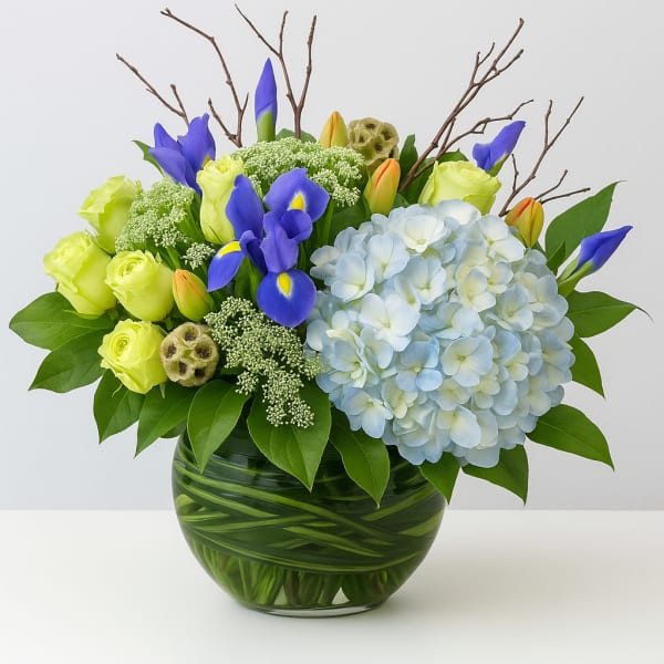 Bouquet of blue irises, pale hydrangea, and lime roses in a glass vase