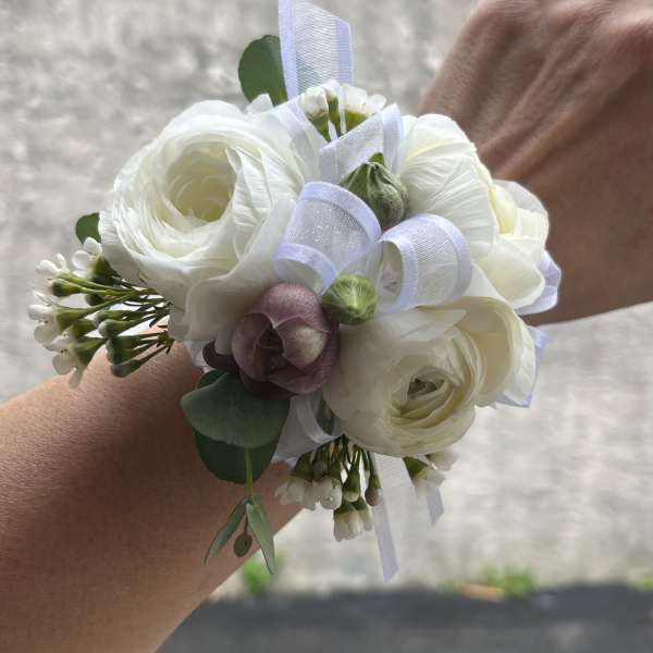 White floral wrist corsage with ribbon and small purple accent flower