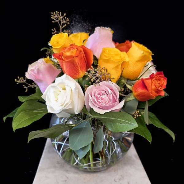 Mixed roses in a clear glass vase with green foliage
