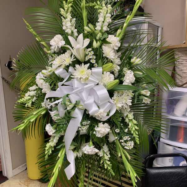 Large white funeral spray with lilies, daisies, and a white ribbon