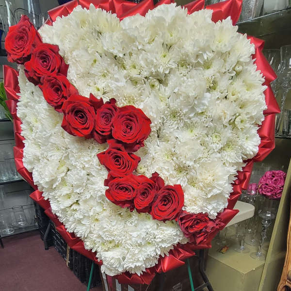 Heart-shaped floral tribute with white chrysanthemums and red roses on a stand