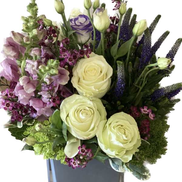Bouquet of cream roses and purple flowers in a square vase