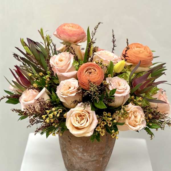 Peach and blush roses with orange ranunculus in a rustic vase