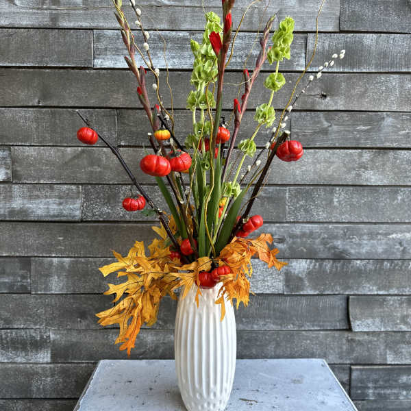 Tall autumn arrangement in a white vase with red and green accents