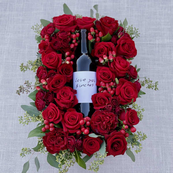 Red roses arranged around a wine bottle with a love note