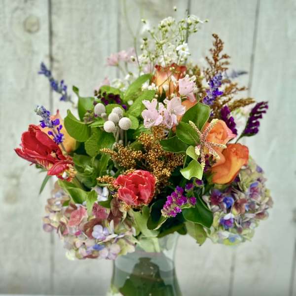 Mixed bouquet of colorful roses, tulips, and hydrangeas in a clear glass vase