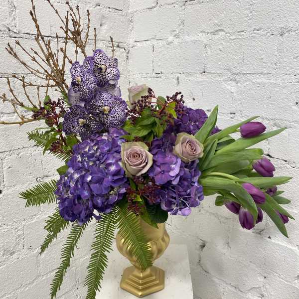 Purple floral arrangement in a gold vase with tulips and orchids