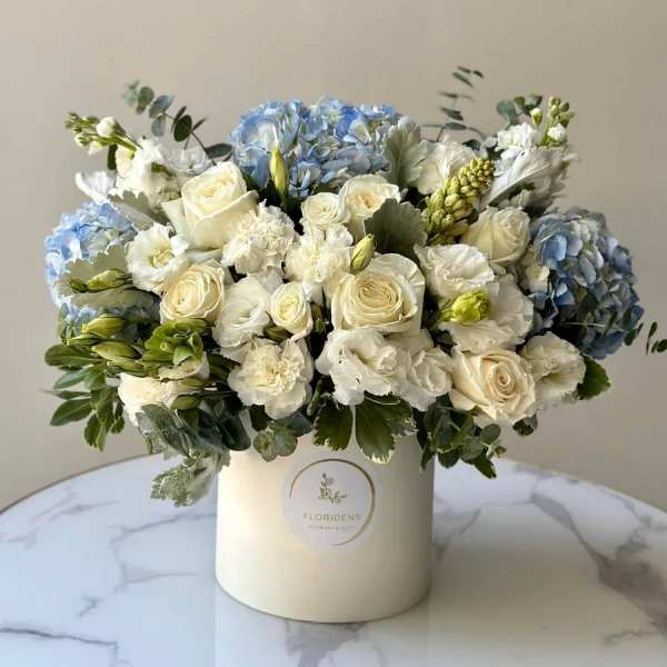 White roses and blue hydrangeas arranged in a cream hatbox