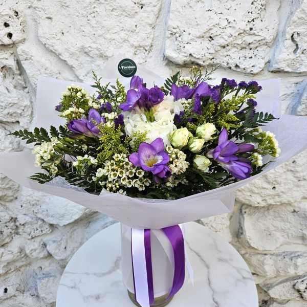 Purple and white bouquet wrapped in paper with a ribbon