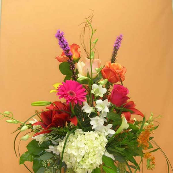 Tall mixed bouquet in a glass vase with pink, red, white, and purple flowers