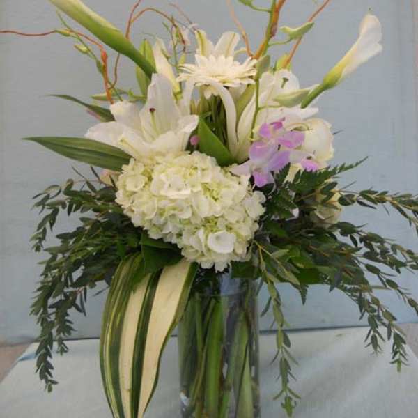 Tall white floral arrangement in a glass vase with orchids and lilies