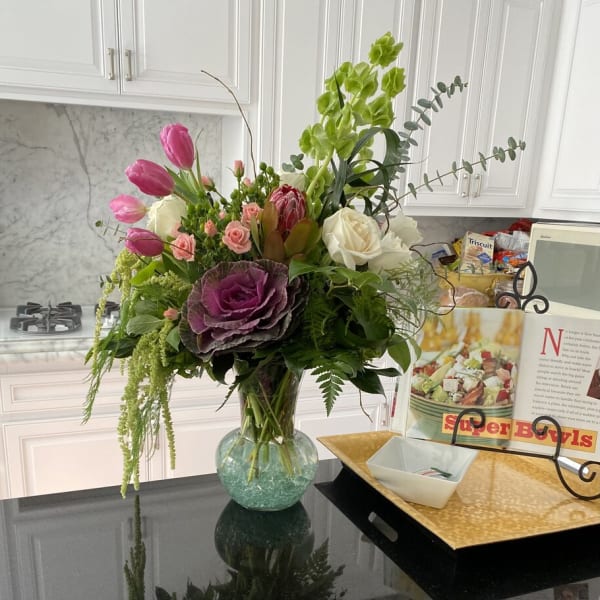 Mixed bouquet of pink tulips, roses, and green orchids in a glass vase