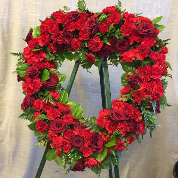 Heart-shaped wreath of red carnations and roses on a stand
