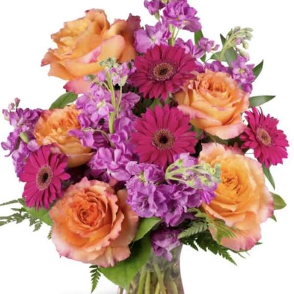 Orange roses and magenta gerbera daisies in a glass vase