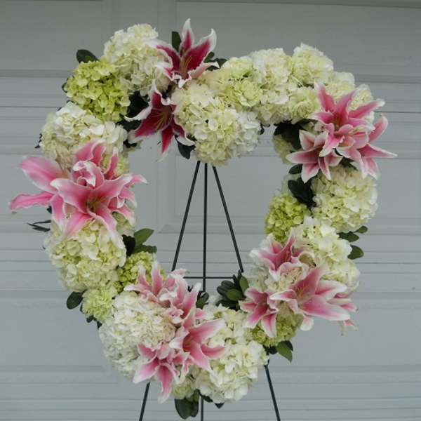 Heart-shaped floral wreath with pink lilies and white hydrangeas on a stand