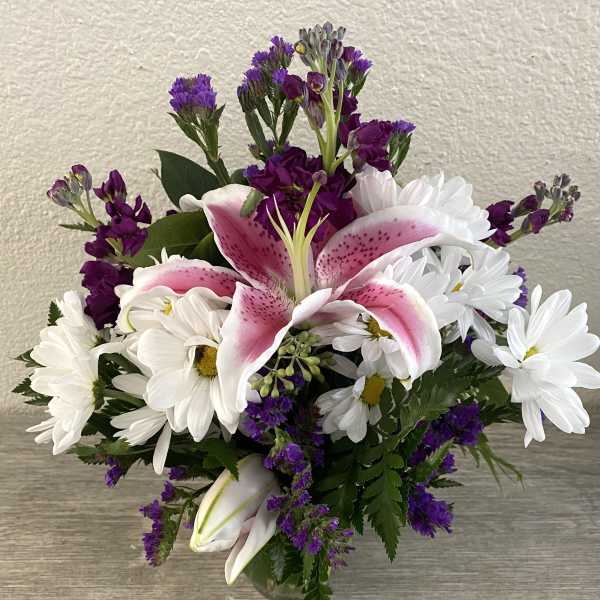 Bouquet of pink lilies and white daisies with purple filler flowers in a glass vase