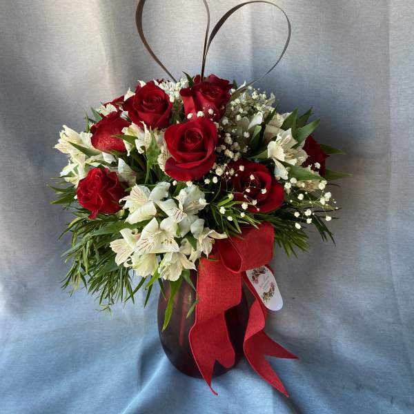 Red roses and white flowers in a dark vase with a red ribbon