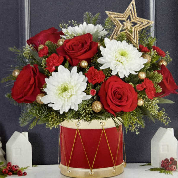 Red roses and white daisies arranged in a red drum vase with gold accents