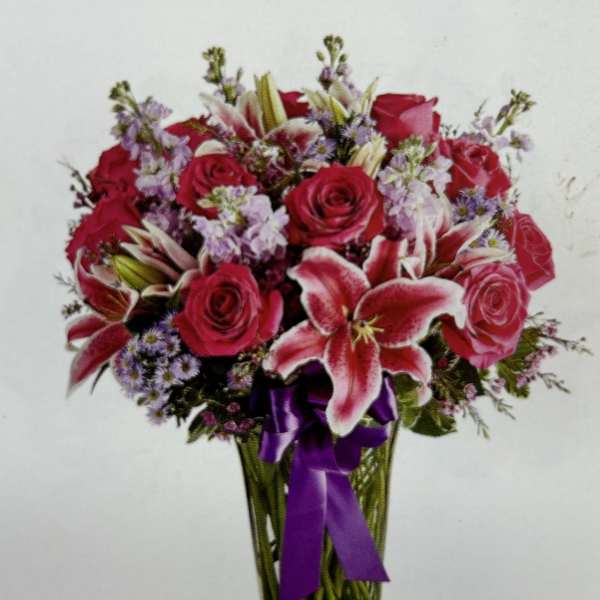 Bouquet of red roses and pink lilies in a glass vase with a purple ribbon
