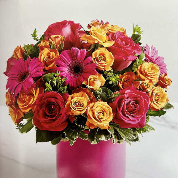 Bouquet of pink, orange, and yellow roses with magenta daisies in a pink vase