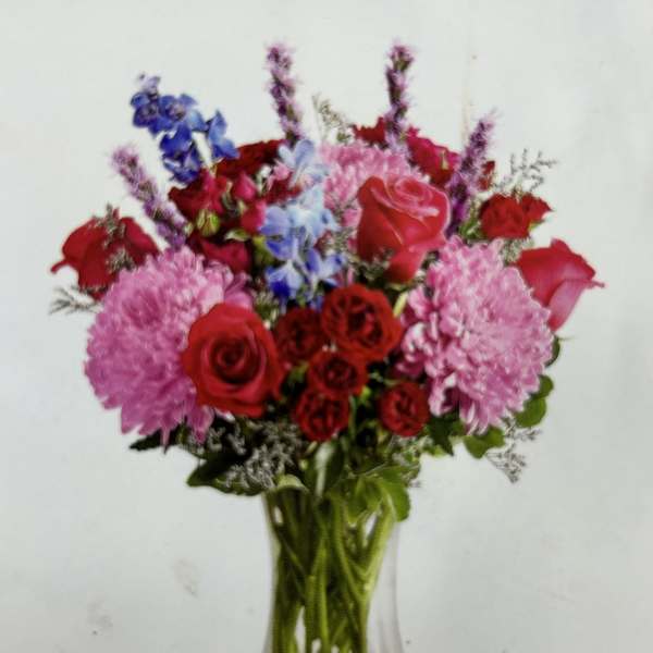 Mixed bouquet of red and pink roses with blue flowers in a glass vase
