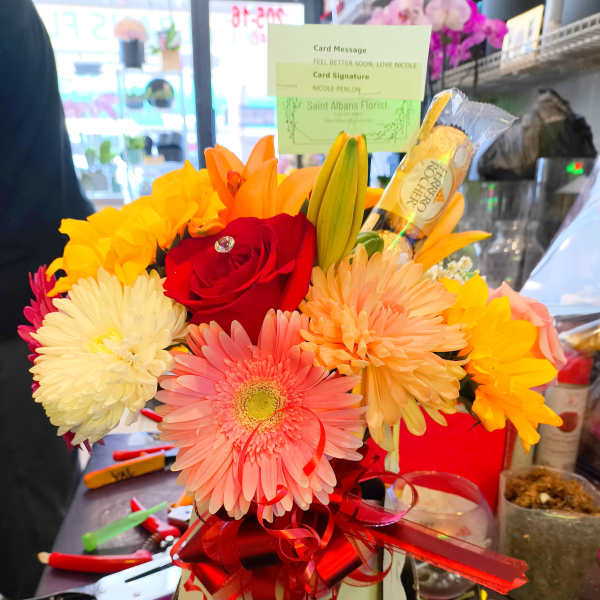 Bright mixed bouquet with a red rose, gerbera daisy, lilies, and chrysanthemums in a gift box.