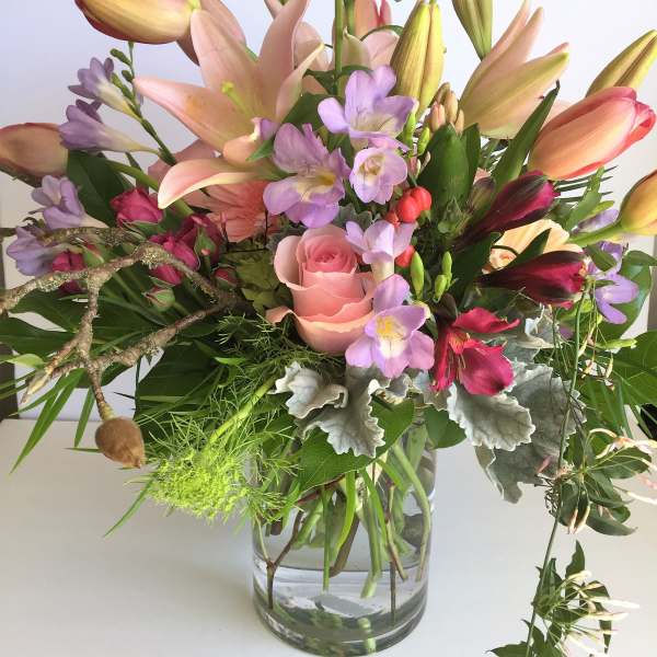 Mixed bouquet with pink roses, lilies, and purple blooms in a glass vase