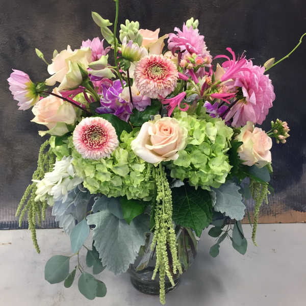 Pink and cream flowers in a glass vase with green hydrangeas