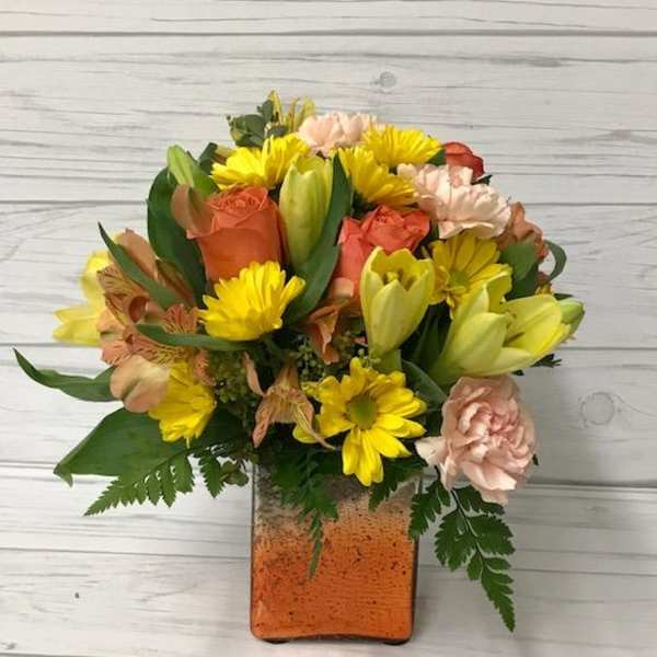 Mixed bouquet of yellow, peach, and coral flowers in a square glass vase