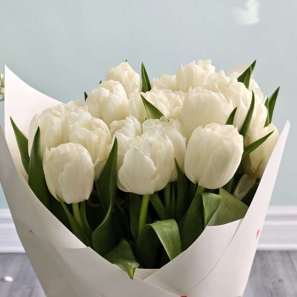 Bouquet of white tulips wrapped in white paper in a glass vase