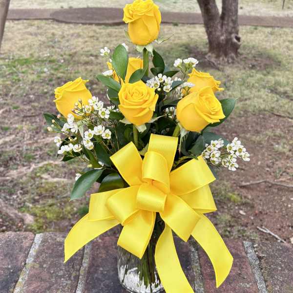 Yellow roses in a clear glass vase with a large yellow ribbon
