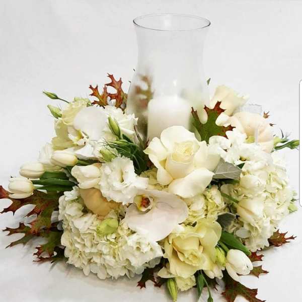 White floral arrangement around a clear glass vase with a candle inside