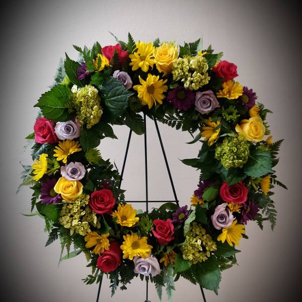 Colorful floral wreath on a black stand with roses and daisies