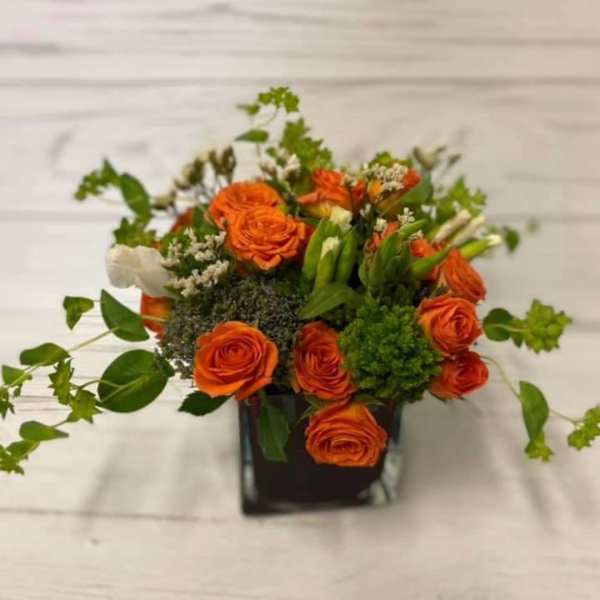 Orange roses arranged in a black square vase with greenery